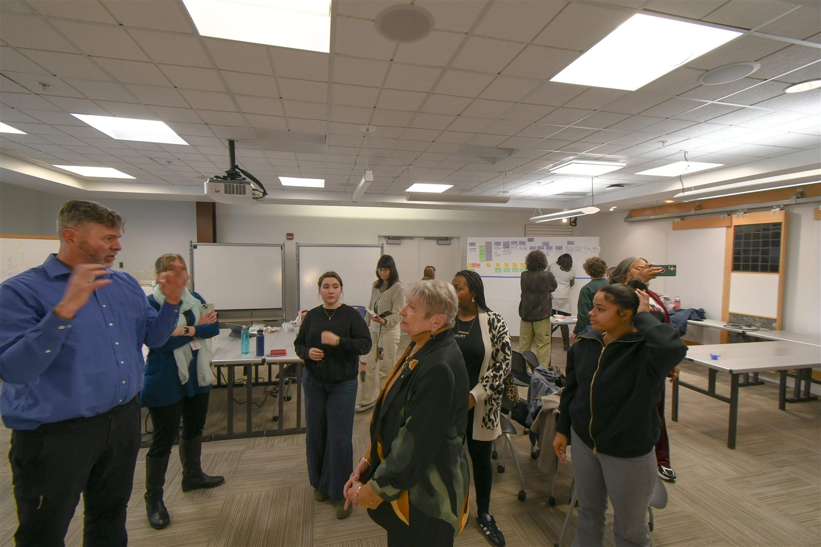 Workshop synthesis session — full group standing and discussing findings in the design studio after completing the service map
