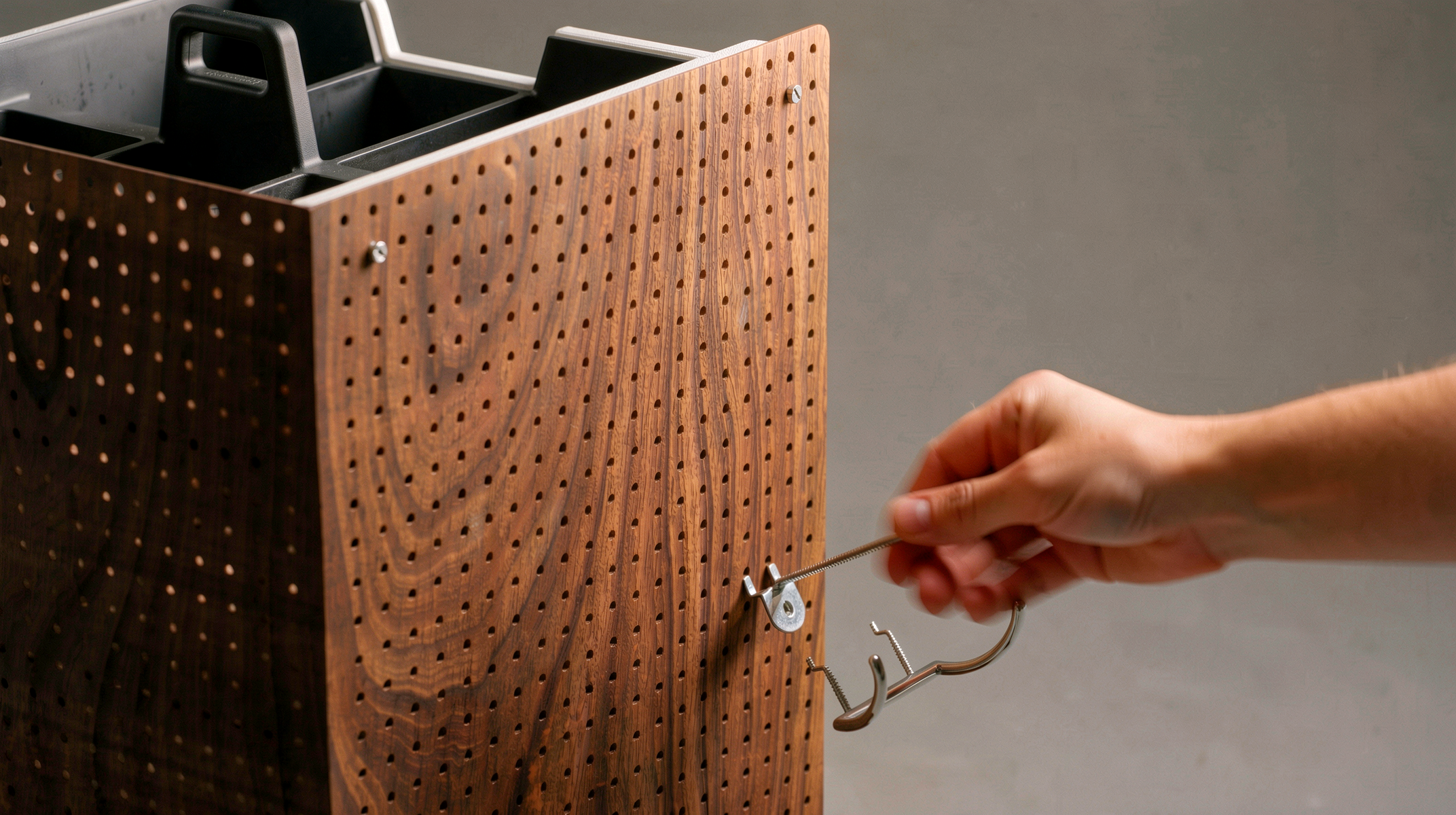 NOMAD DRAWER — hand placing steel hook on walnut pegboard panel, interaction detail